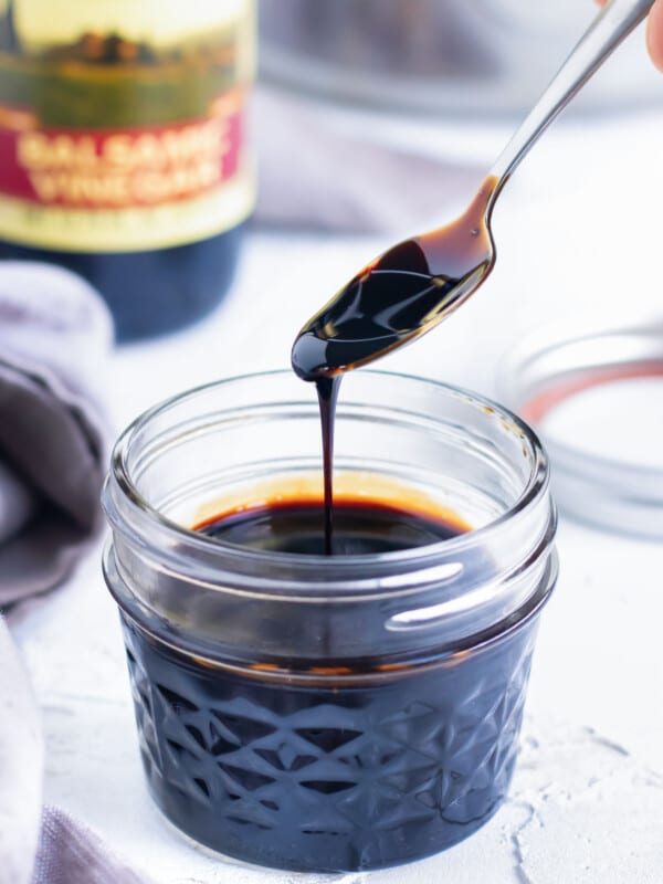 A healthy balsamic glaze recipe being scooped up from a glass jar with a spoon.