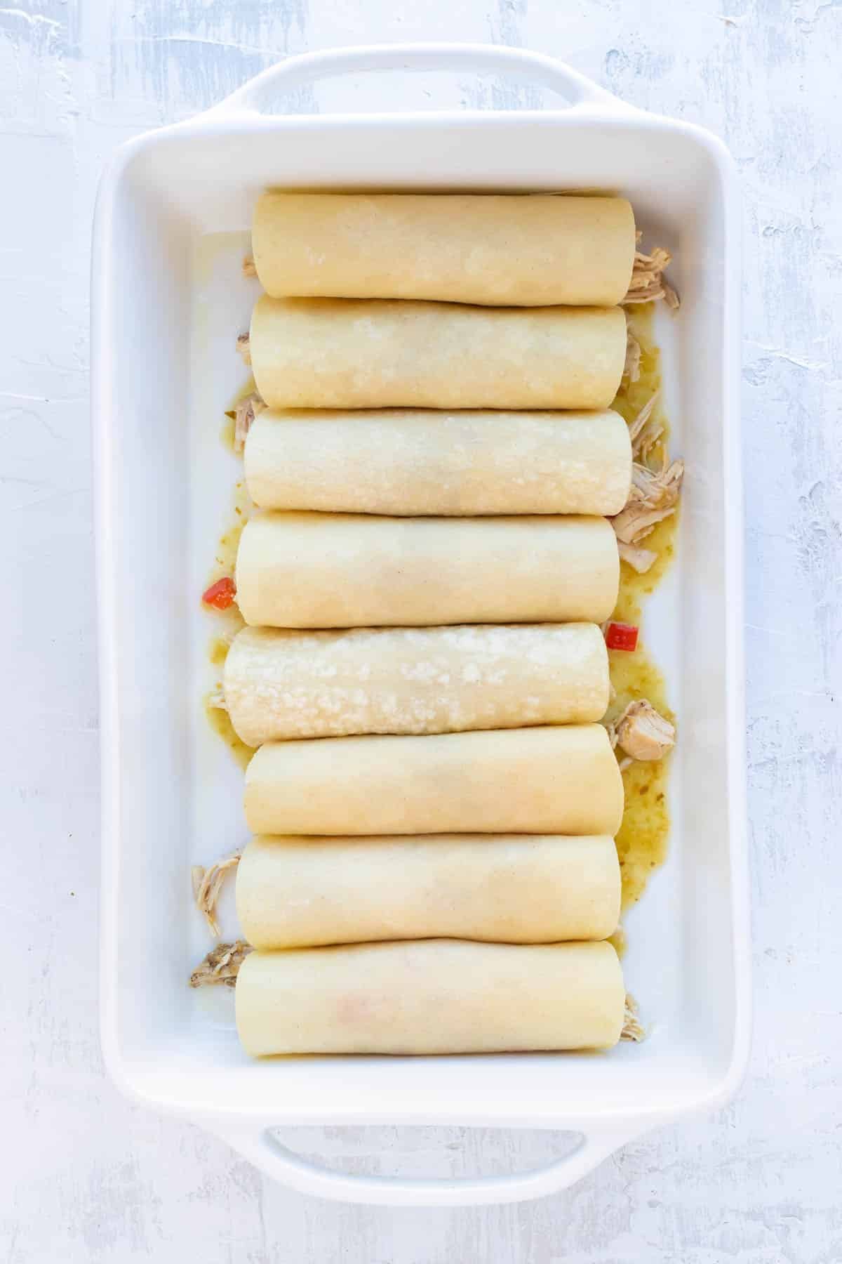 Rolled enchiladas are lined up in a casserole dish.