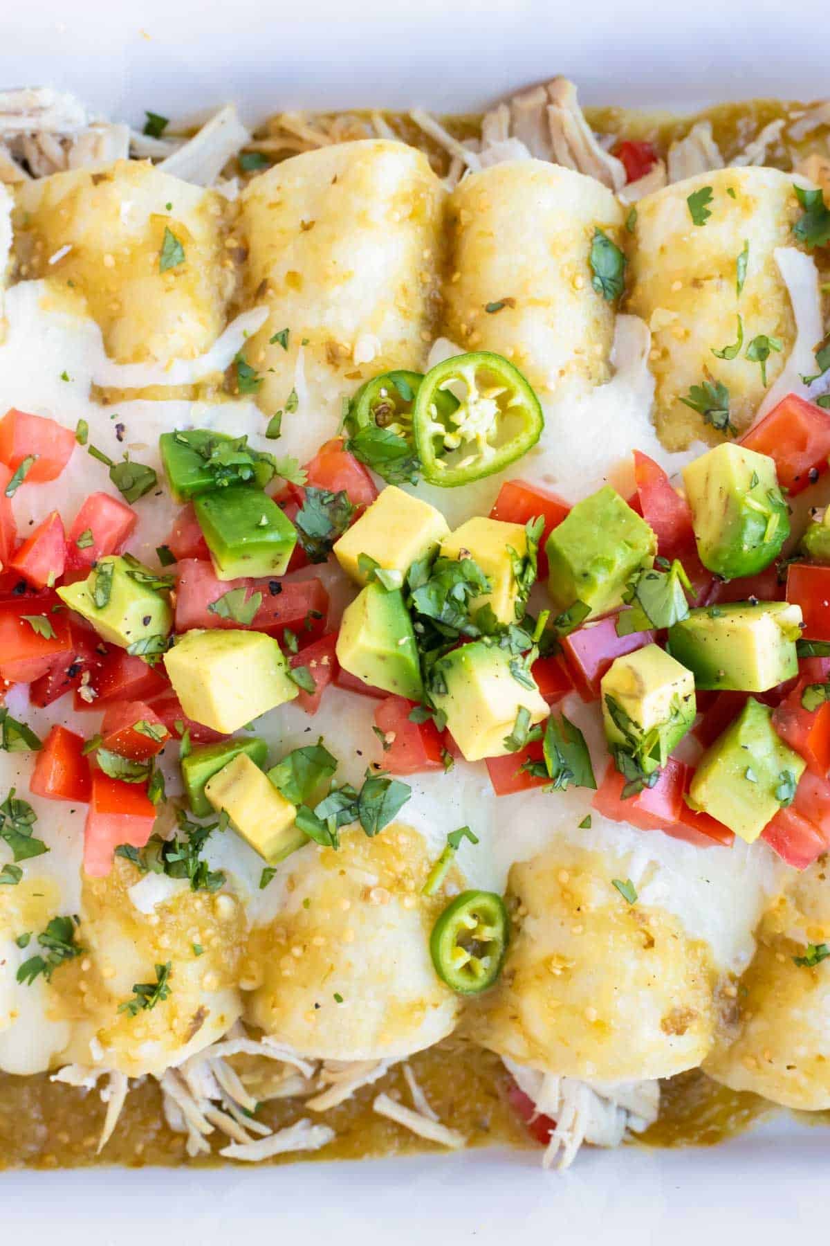 Healthy enchiladas with salsa verde and shredded chicken in a white pan.