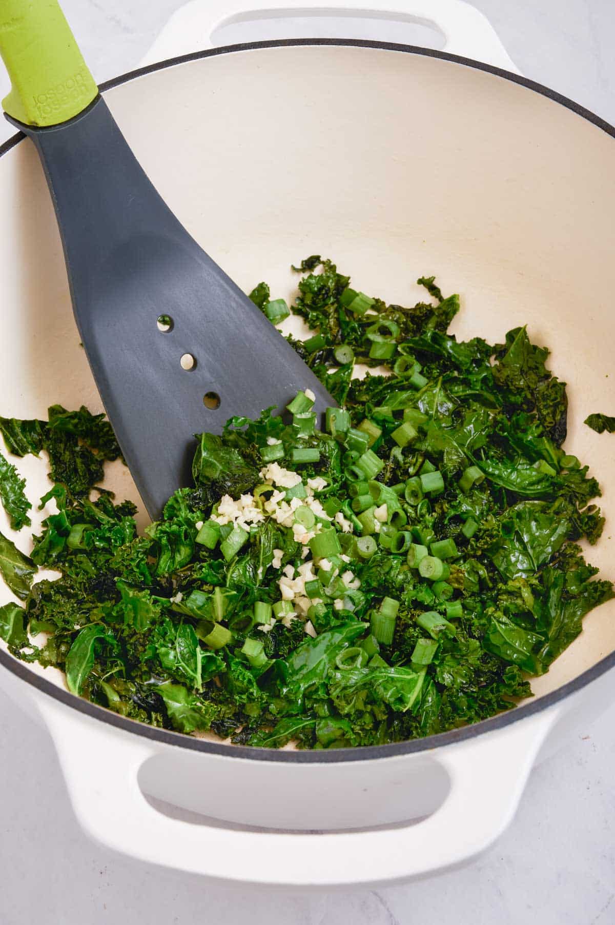 A spatula stirs cooking kale with garlic.