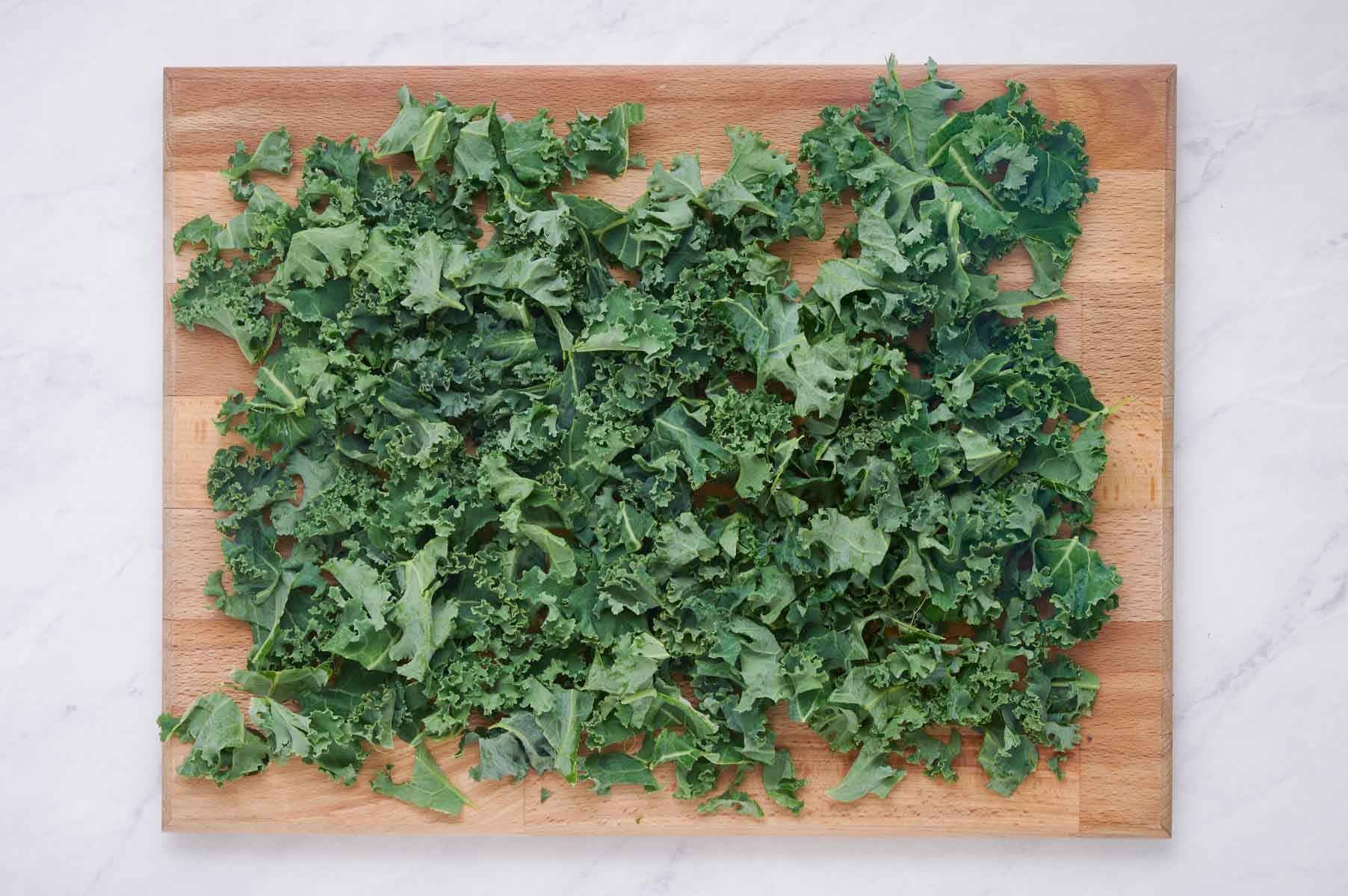A cutting board is full of chopped kale.
