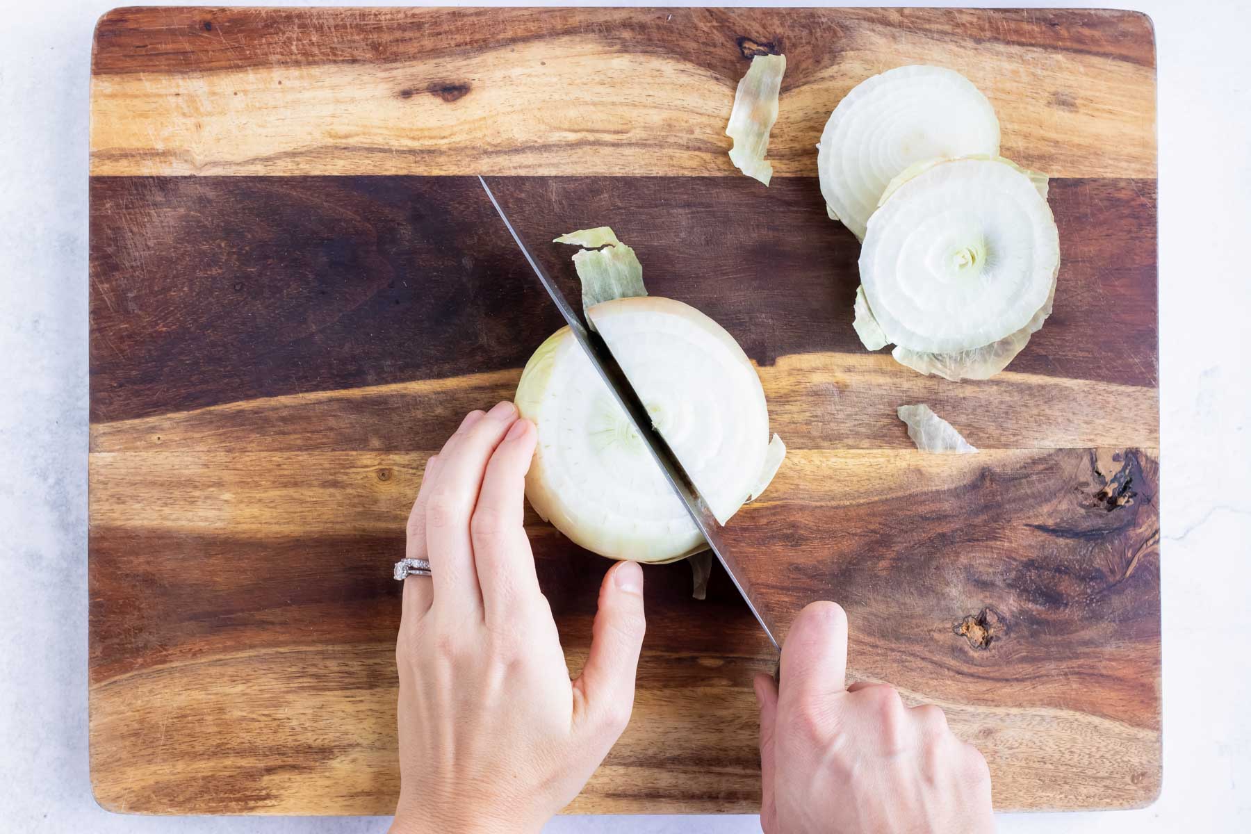 The onion is cut in half on a wooden cutting board and a knife. 