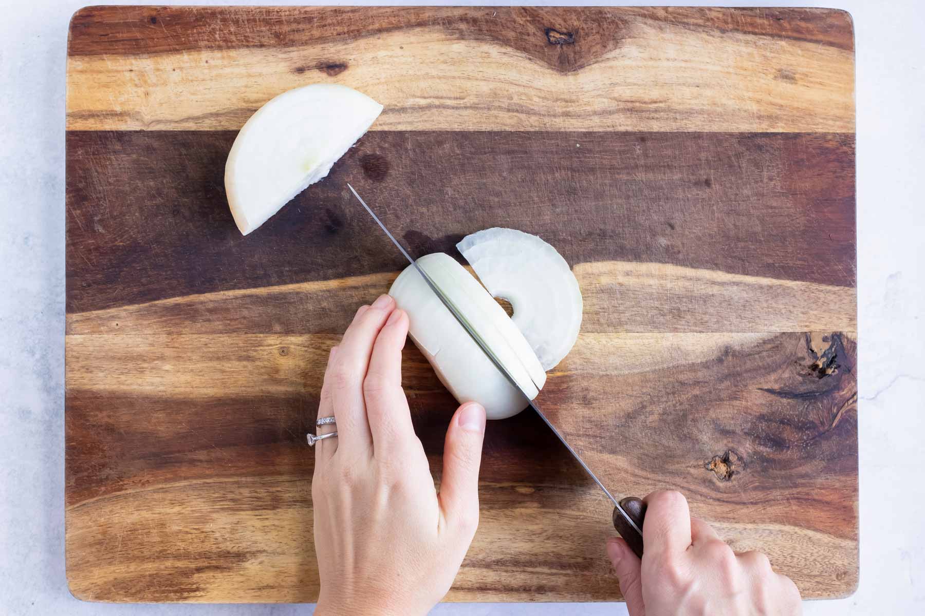 Onion on a cutting board being cut into slices.