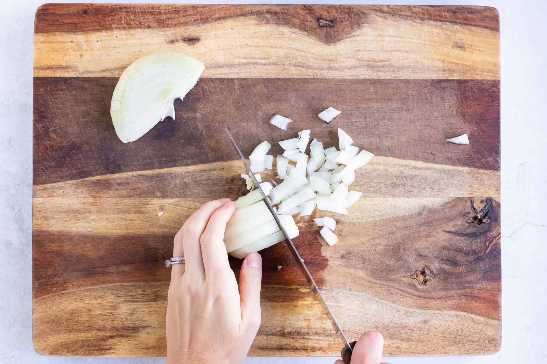 Onion slices are diced into small pieces on a cutting board.