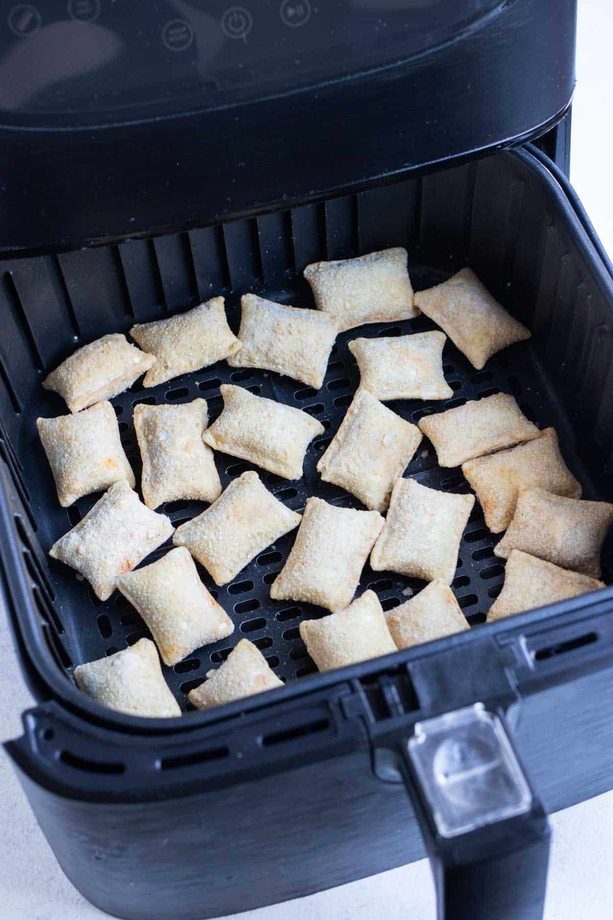 Uncooked pizza rolls are in an air fryer.