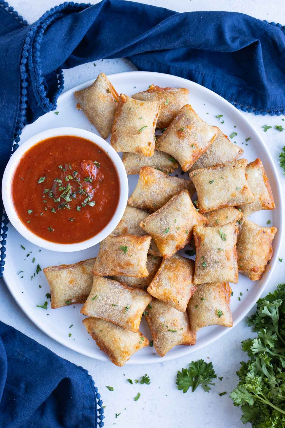 Pizza rolls are served on a white plate with a bowl of marinara sauce.