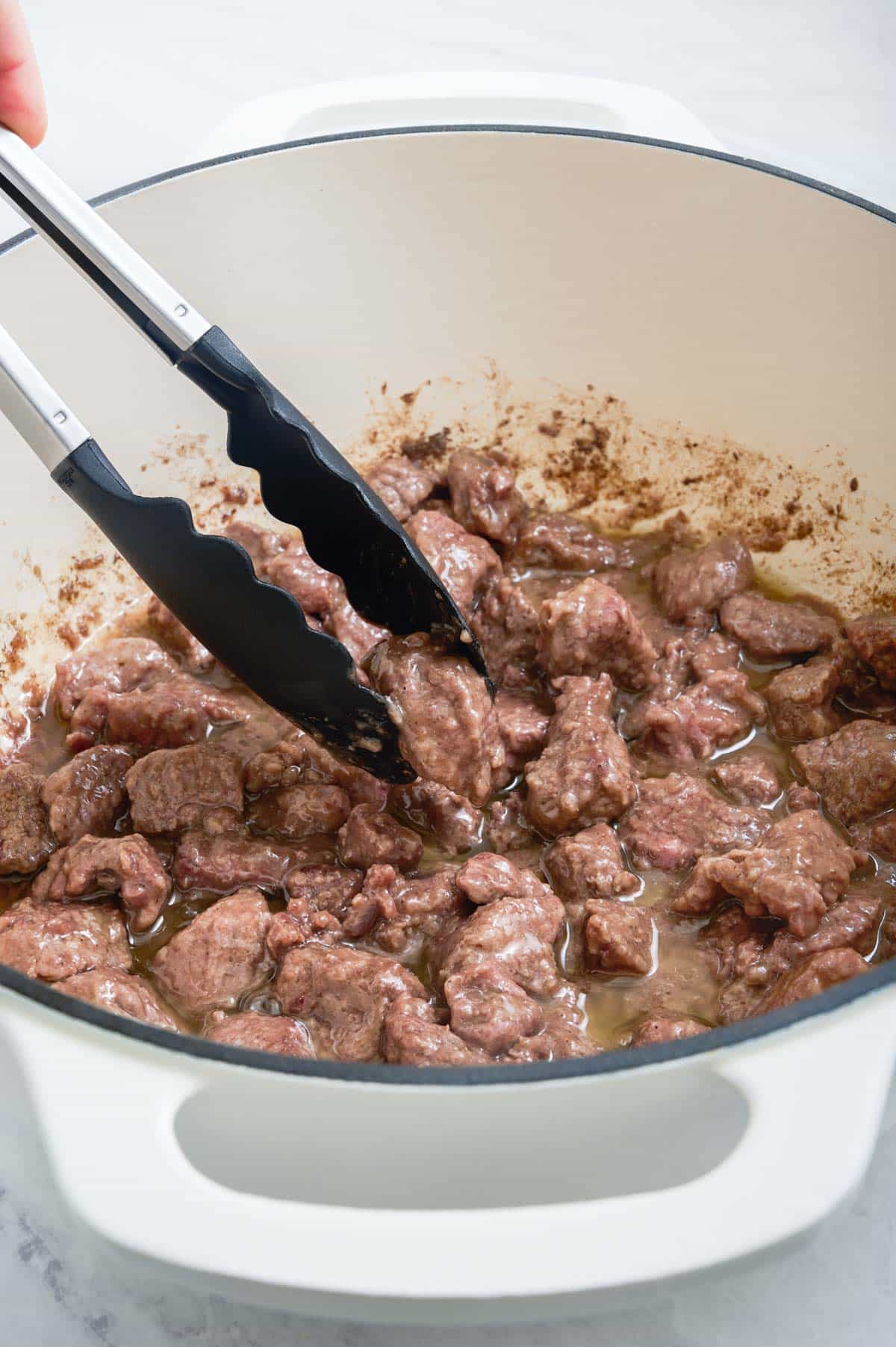 Tongs stir meat that is cooking.