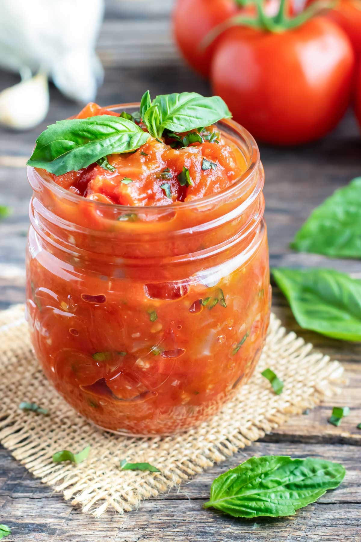 Homemade spaghetti sauce in a clear jar with basil and tomatoes around it.