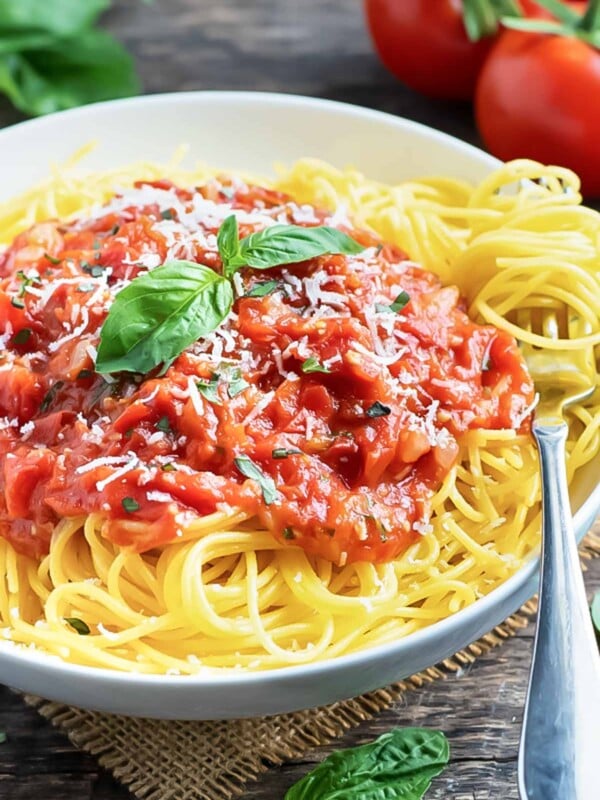 A white bowl full of spaghetti with pasta pomodoro sauce and basil.