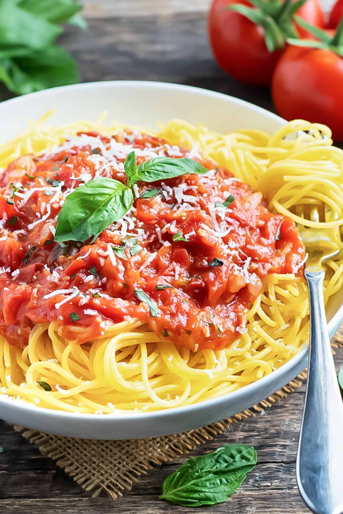 A white bowl full of spaghetti with pasta pomodoro sauce and basil.