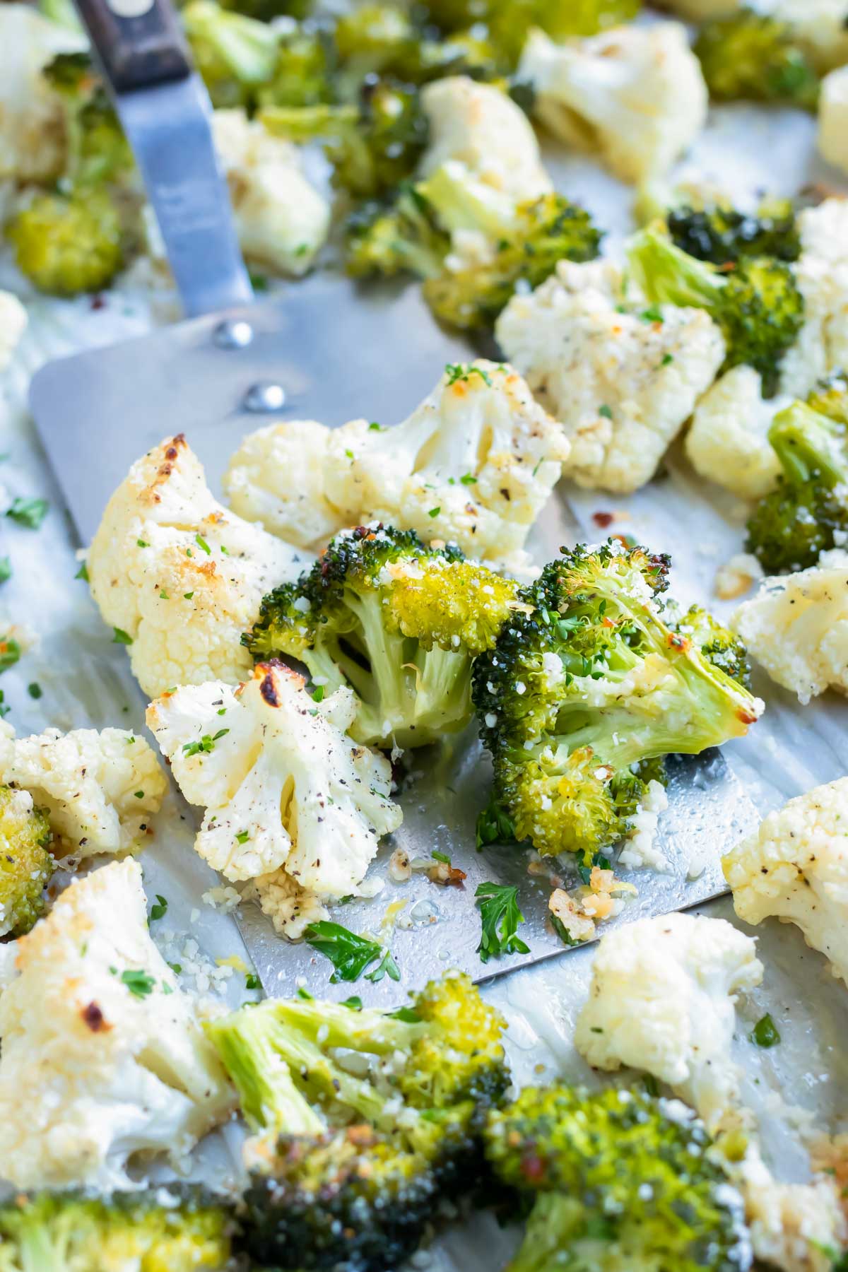 Parmesan roasted broccoli and cauliflower are baked on parchment paper for easy removal from the oven.