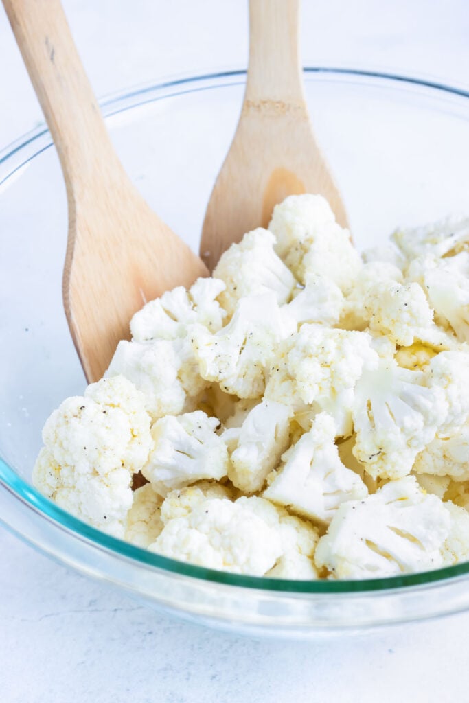 Cauliflower florets tossed with garlic butter and grated Parmesan in a glass bowl.