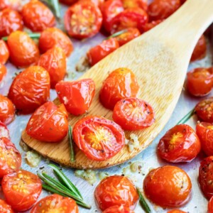 A wooden spatula scooping up roasted cherry tomatoes from a baking sheet.
