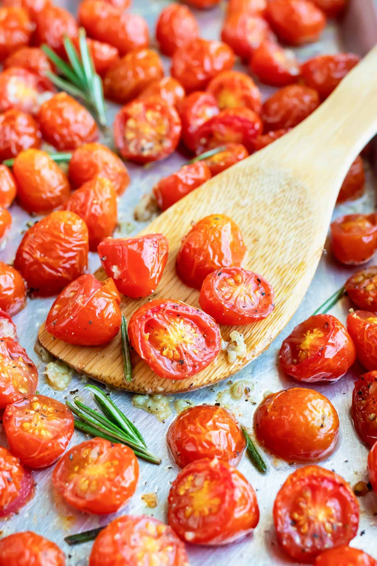 A wooden spatula scooping up roasted cherry tomatoes from a baking sheet.