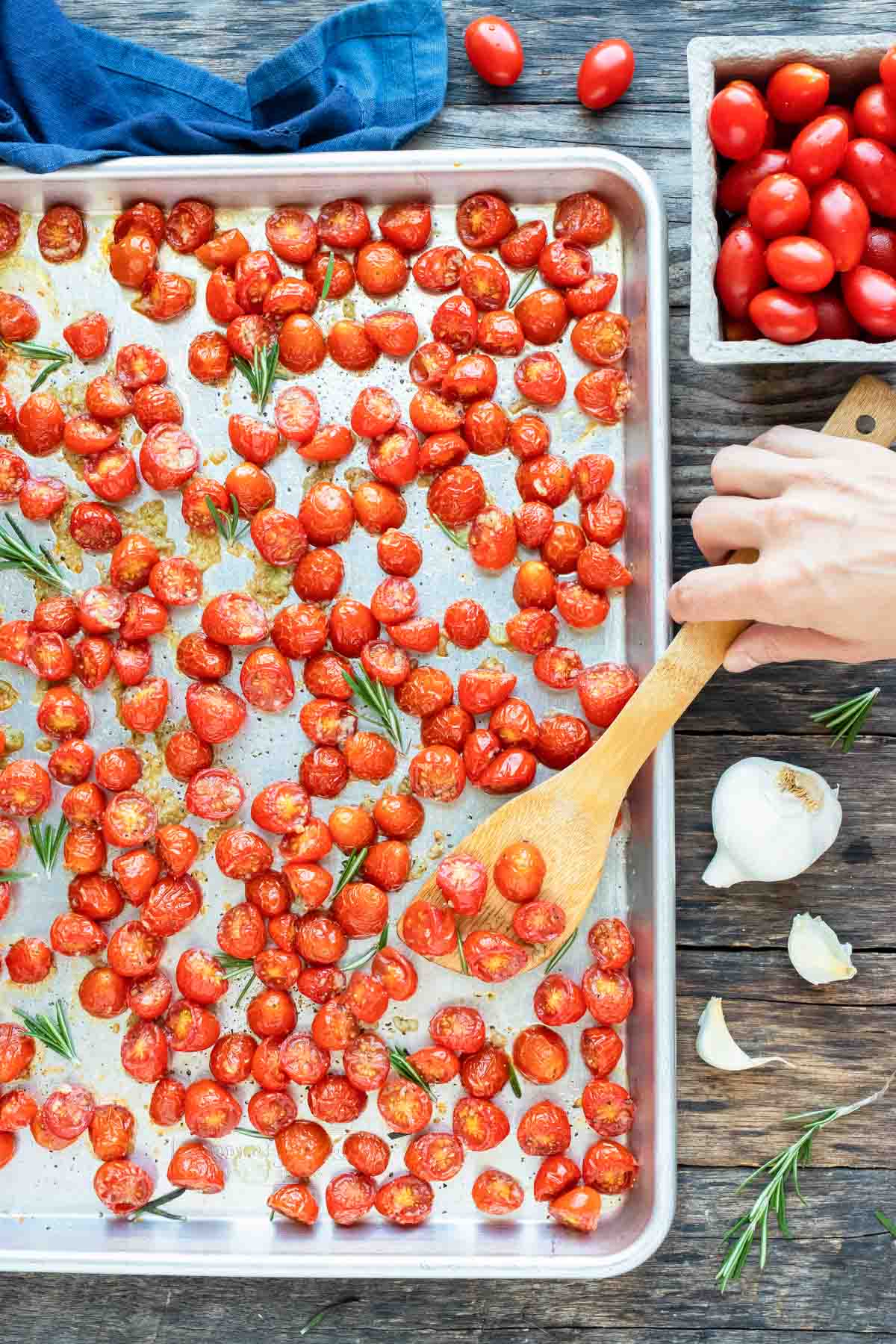 Roasted cherry tomatoes on a large baking sheet with a hand scooping up some.