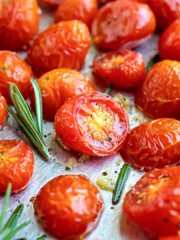 Roasted cherry tomatoes on a baking sheet with rosemary next to it.