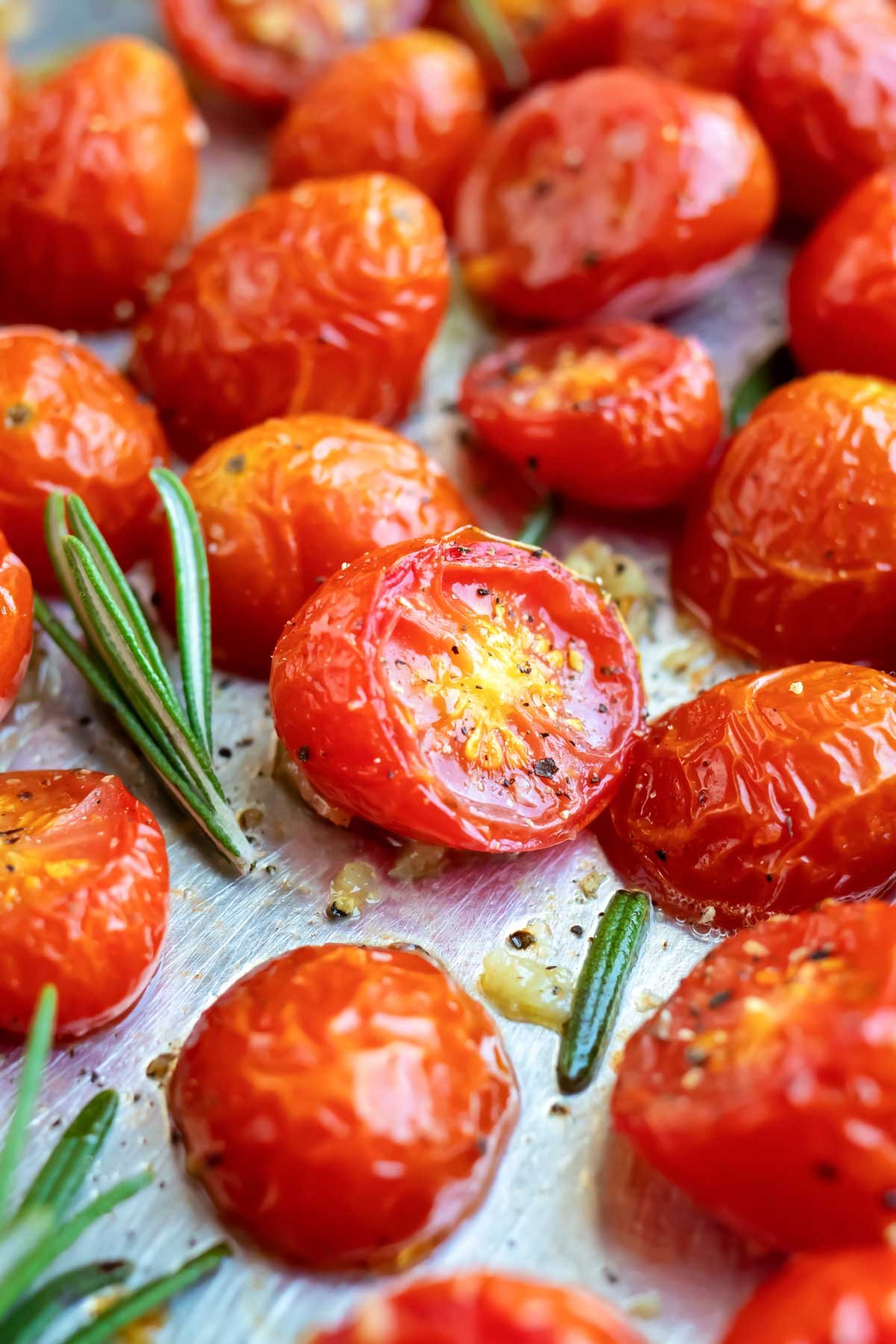 Roasted cherry tomatoes on a baking sheet with rosemary next to it.