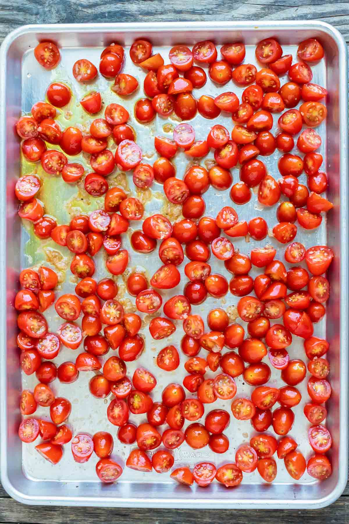 Tomato halves and garlic in a single layer on a baking sheet.