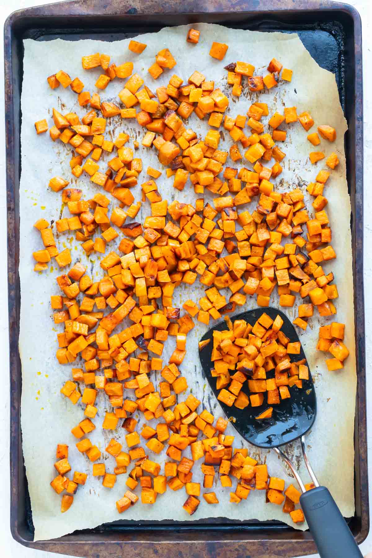 Roasted sweet potato cubes on a sheet pan with parchment paper.