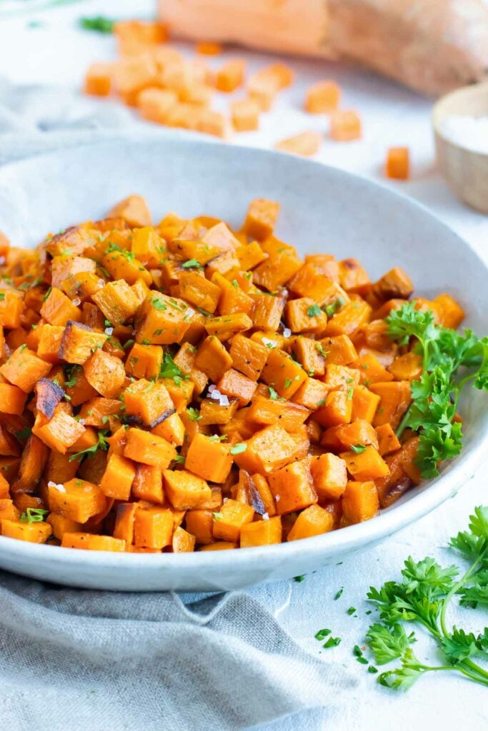 Baked sweet potato cubes are in a bowl next to cilantro.