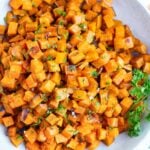 Roasted sweet potato cubes are served in a white bowl after baking in the oven.