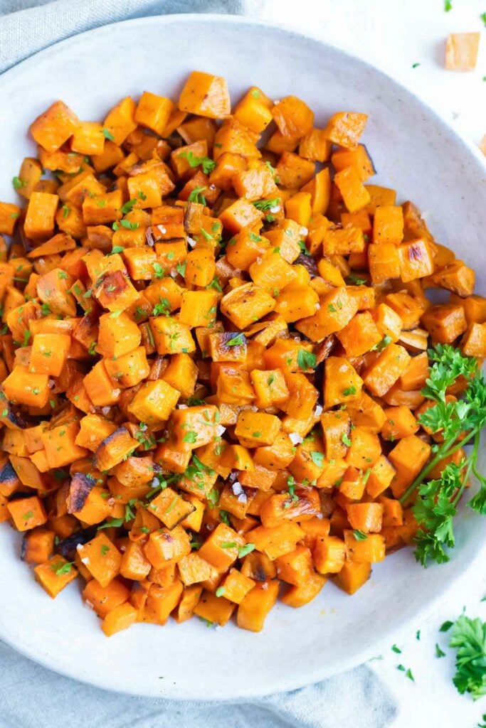 Roasted sweet potato cubes are served in a white bowl after baking in the oven.
