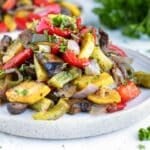 A pile of oven-roasted vegetables on a white plate with another serving in the background.