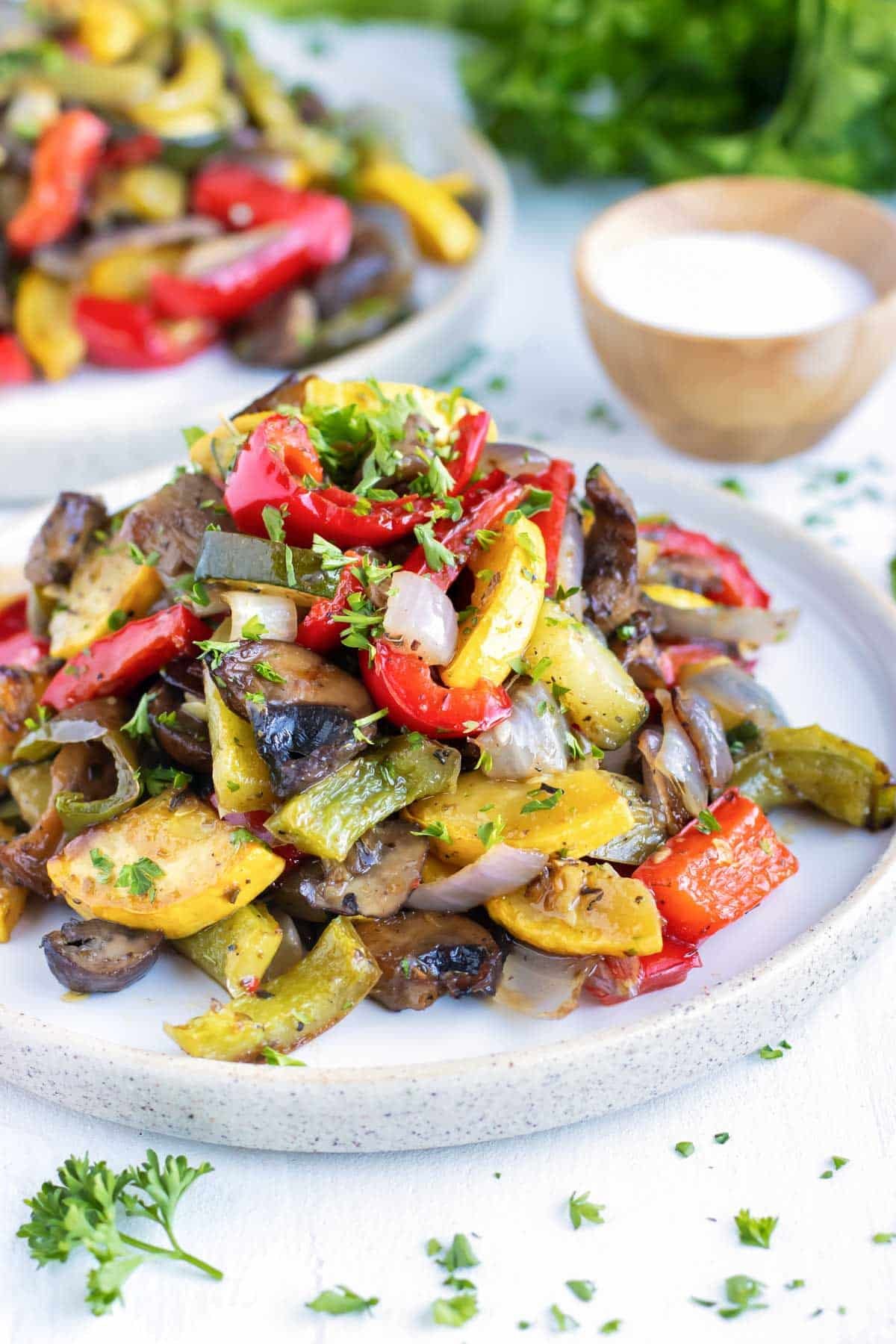 A pile of oven-roasted vegetables on a white plate with another serving in the background.