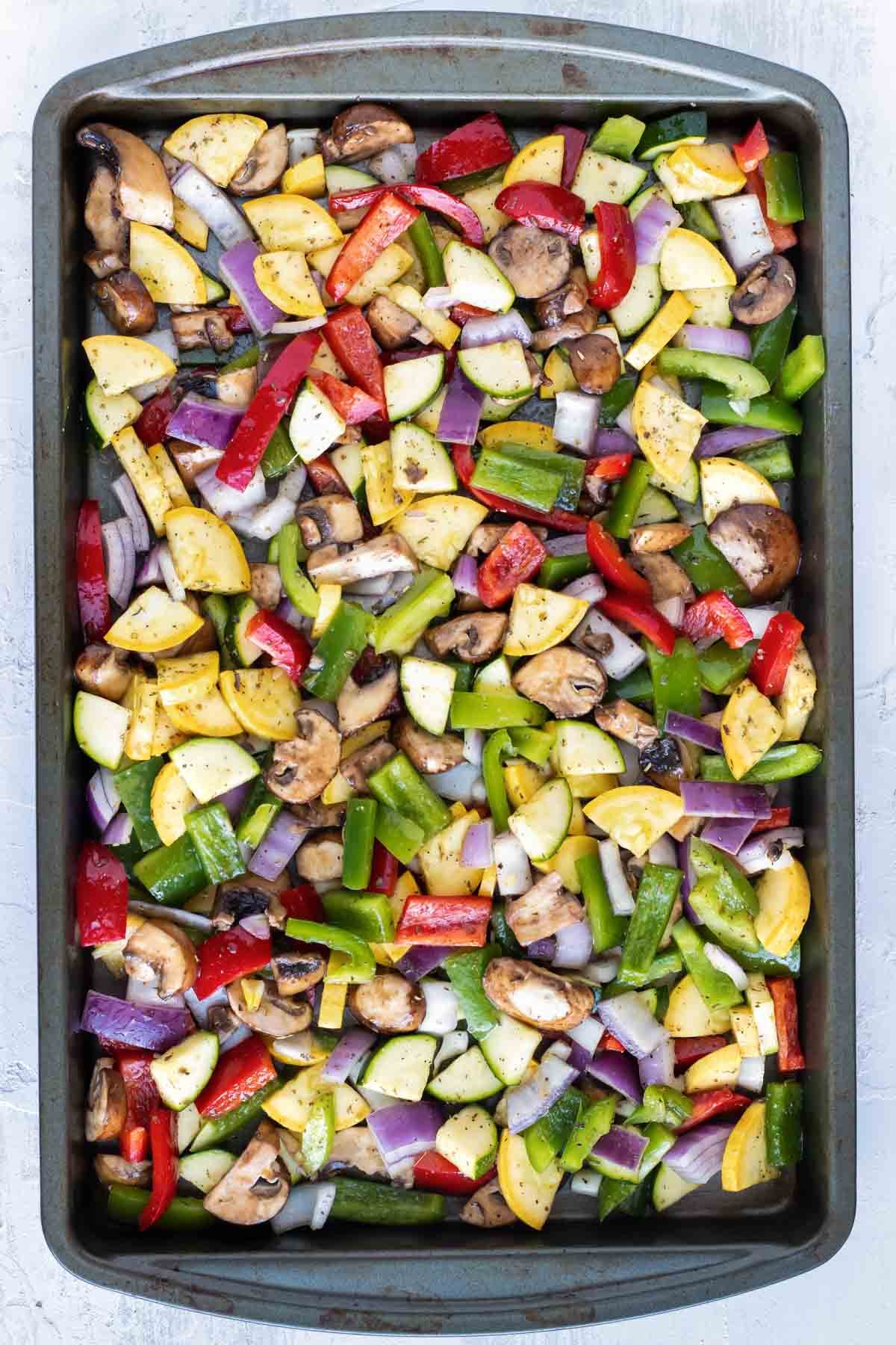 Raw veggies are spread on a baking sheet.