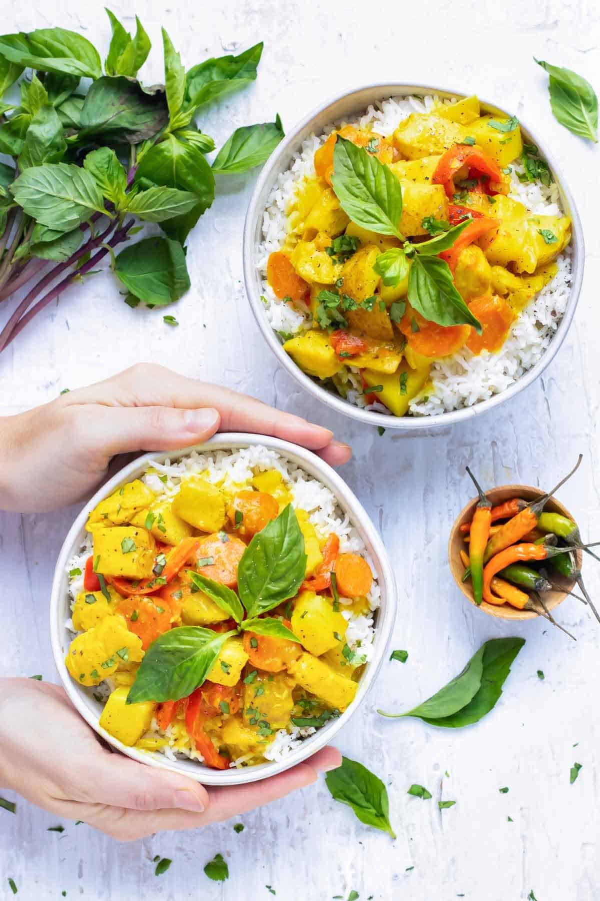 Two bowls full of a coconut curry recipe with Thai chili peppers next to it.