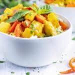 A white serving bowl of Thai curry that is made with yellow curry paste, chicken, potatoes, and carrots.