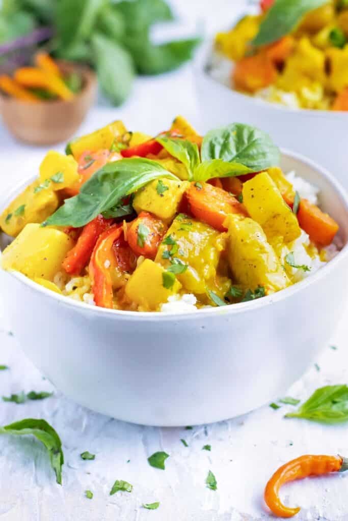 A white serving bowl of Thai curry that is made with yellow curry paste, chicken, potatoes, and carrots.