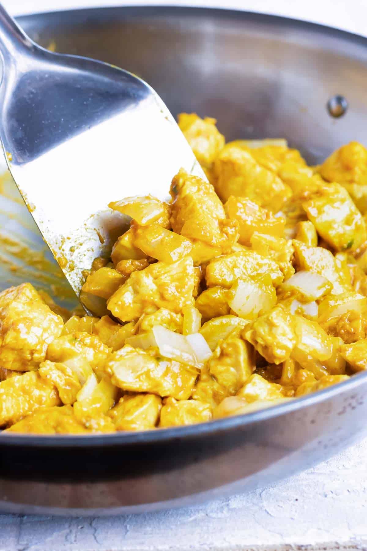 A spatula stirs the chicken, curry, and coconut milk.