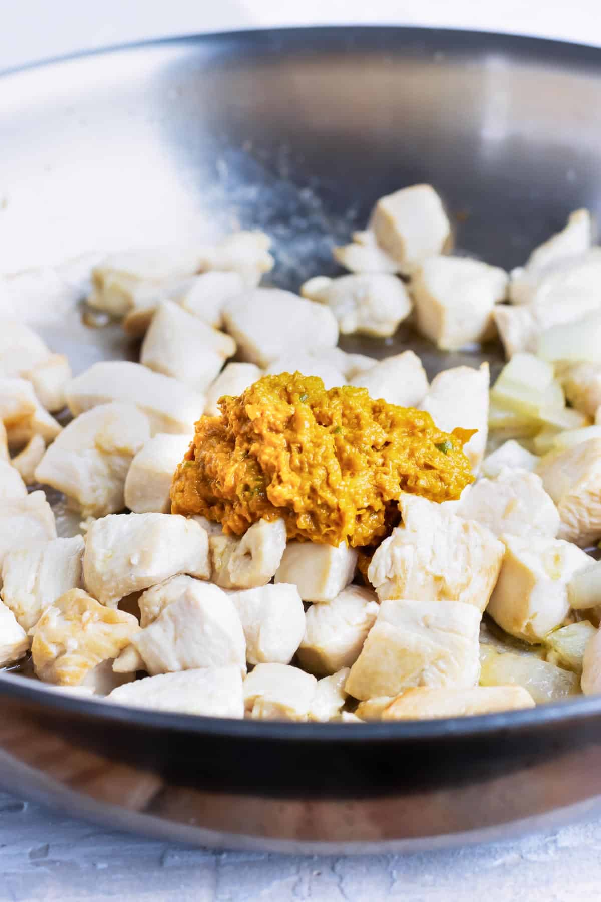 Yellow curry paste is added to cooked chicken cubes.