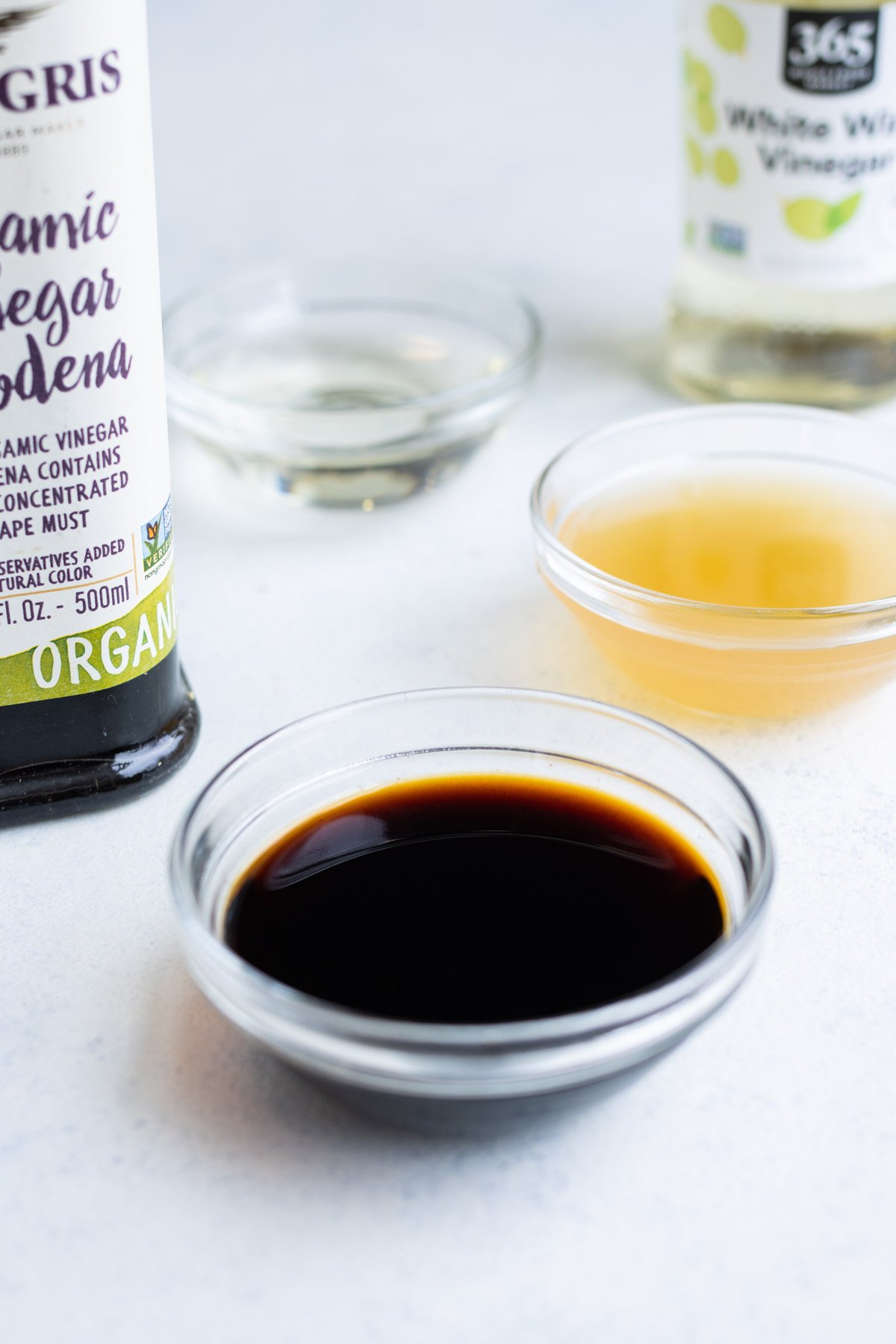 Close-up of balsamic vinegar in a small, glass bowl with other vinegars in the background.