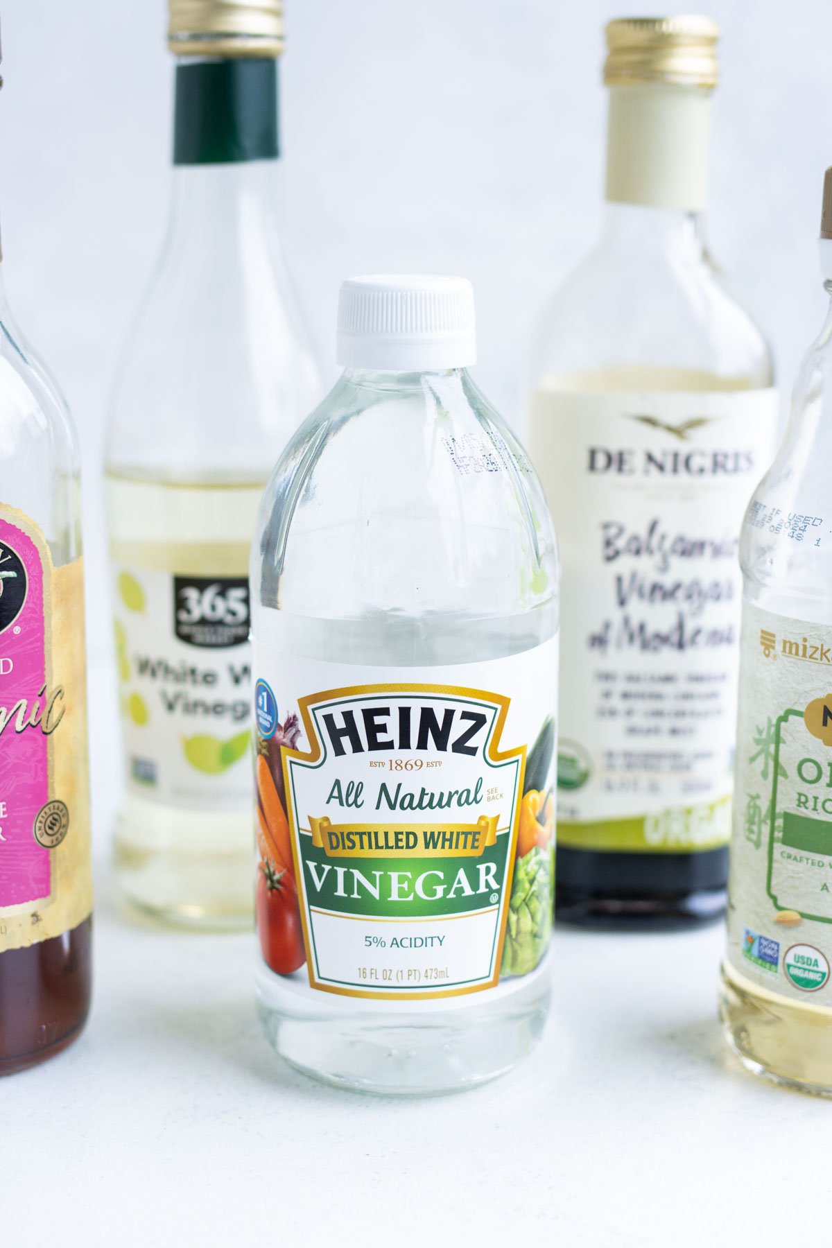 Zoomed-in distilled white vinegar with an assortment of other vinegars surrounding it.