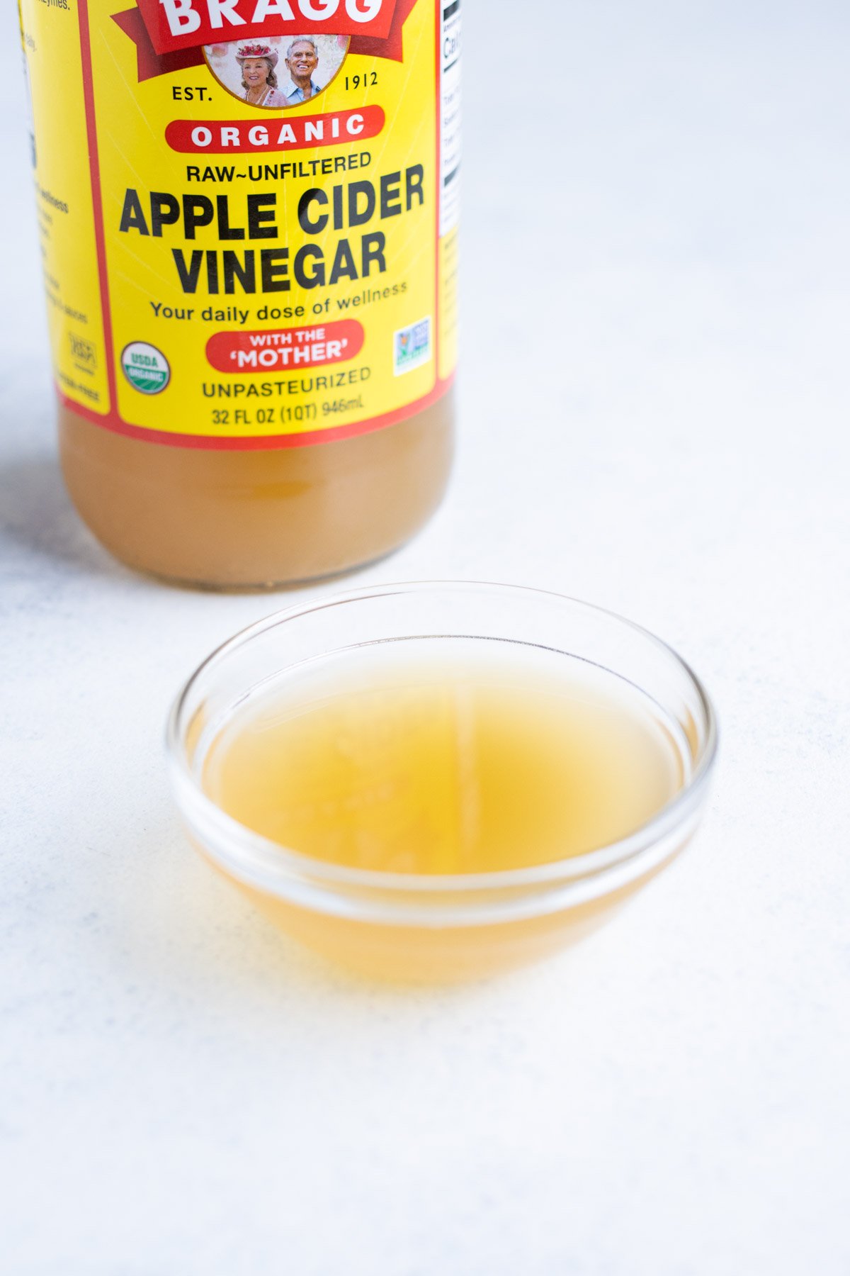 Apple cider vinegar in a small glass bowl with the container in the background.