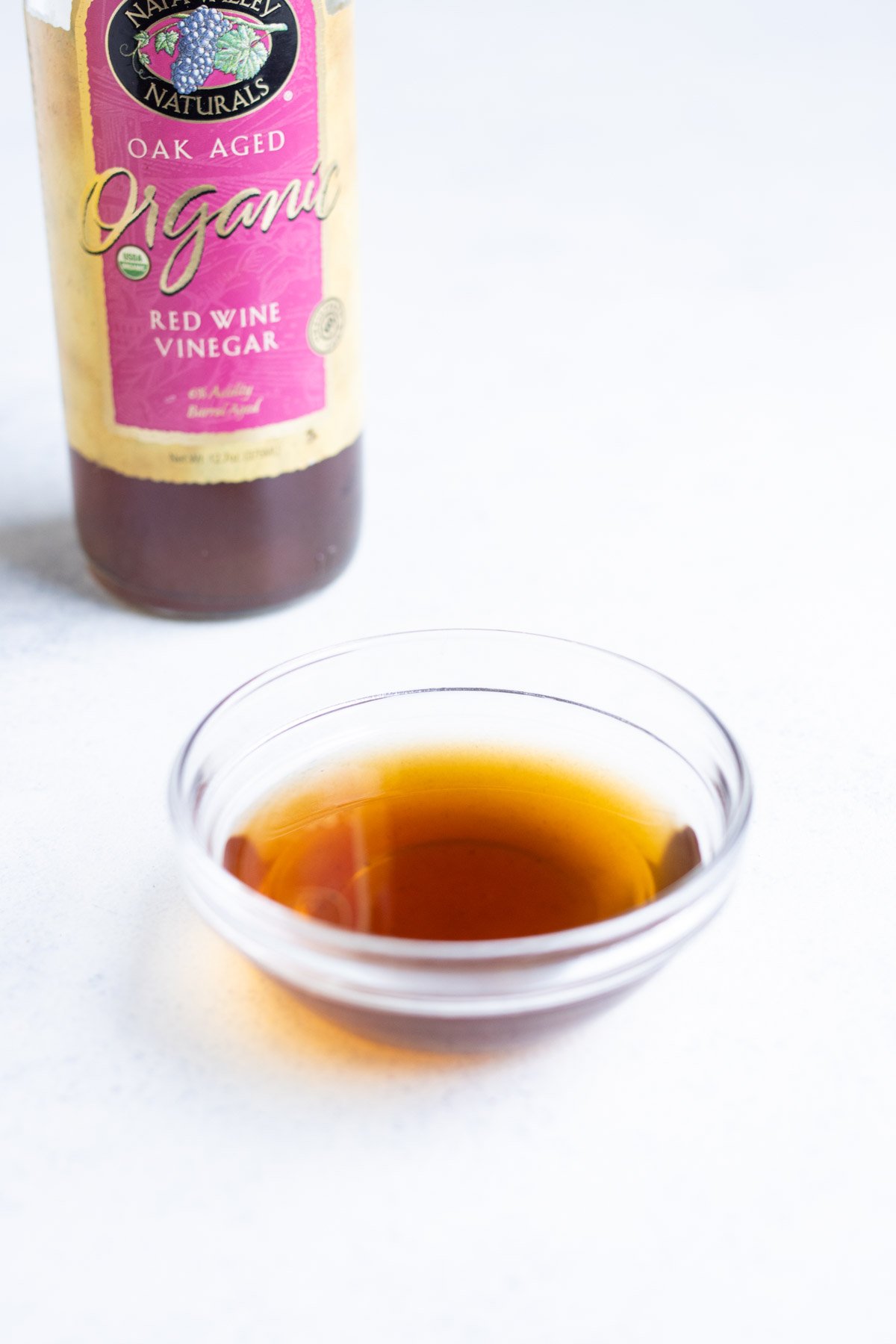 Red wine vinegar in a small glass bowl with the container in the background.