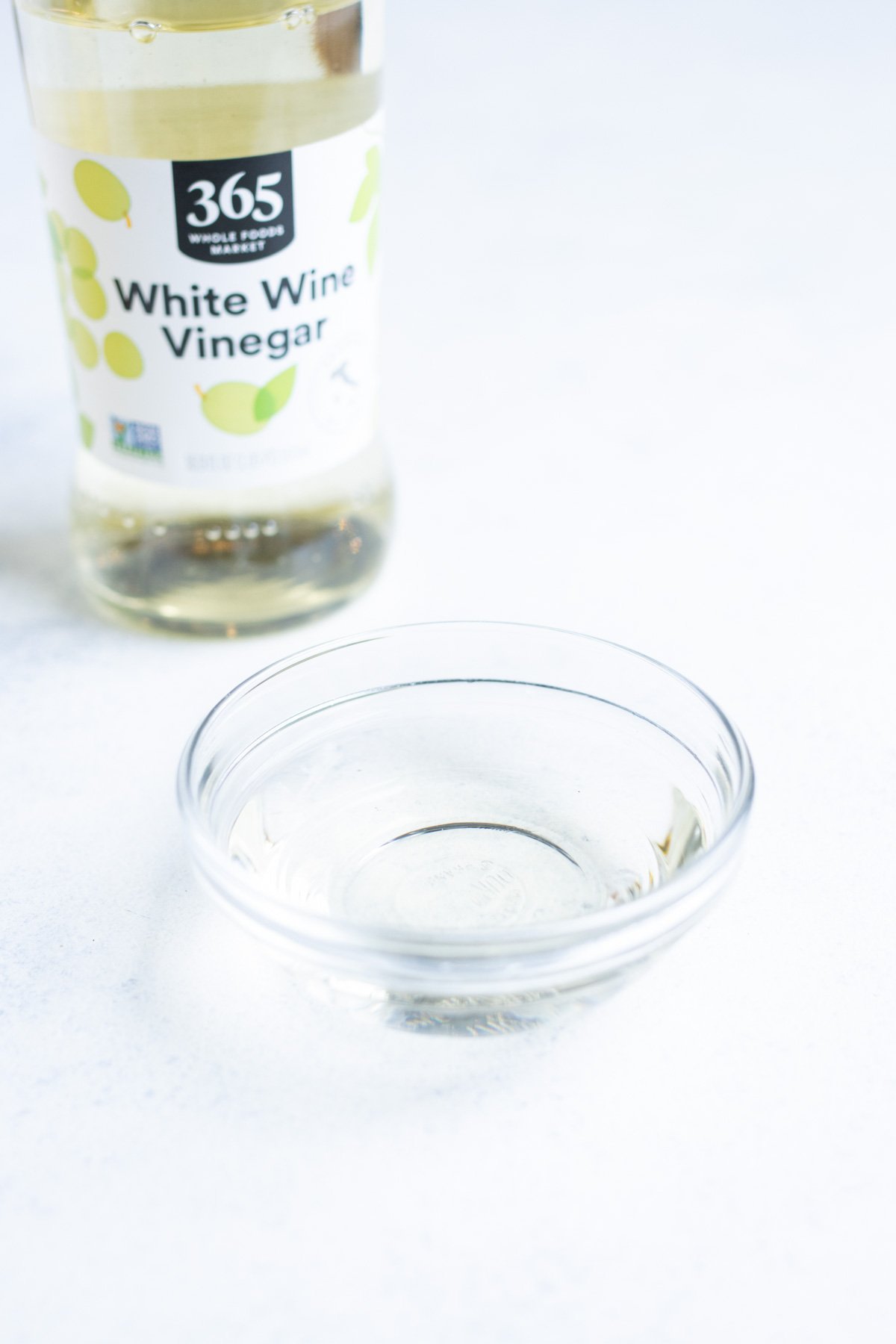 White wine vinegar in a small glass bowl with the container in the background.