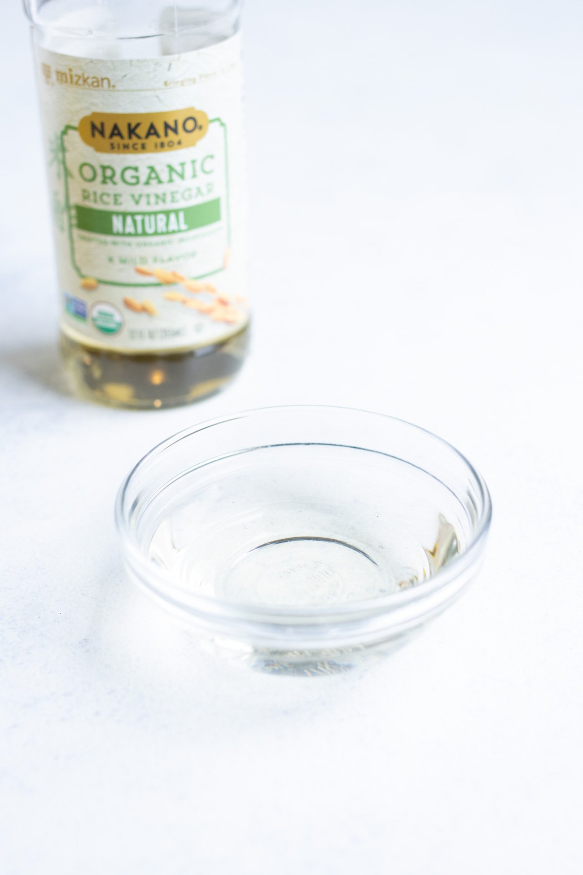 Organic rice wine vinegar in a small glass bowl with the container in the background.