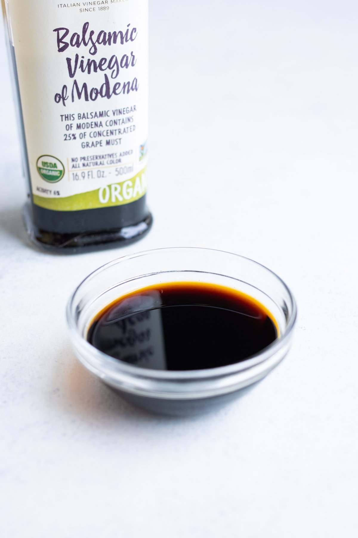 Balsamic vinegar in a small glass bowl with the container in the background.