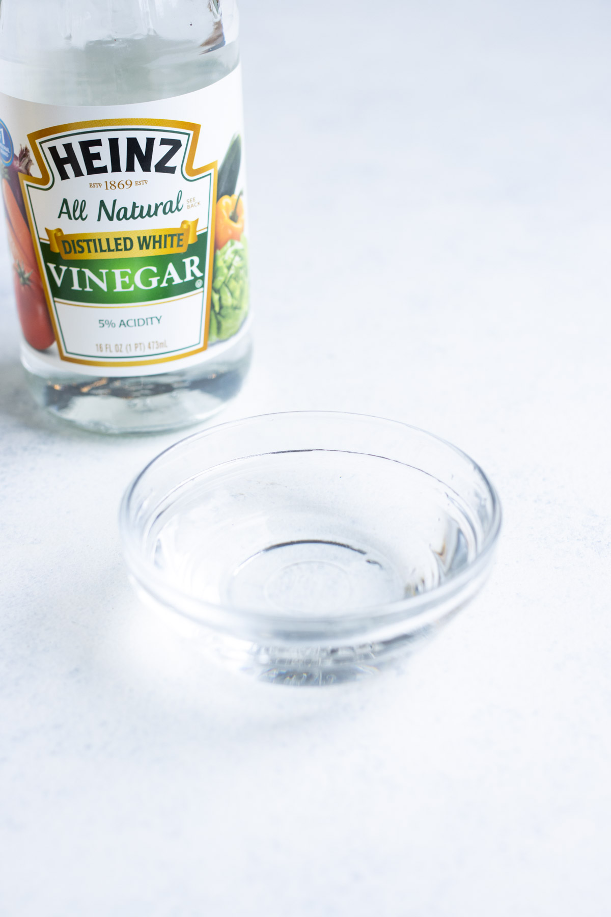 Distilled white vinegar in a small glass bowl with the container in the background.
