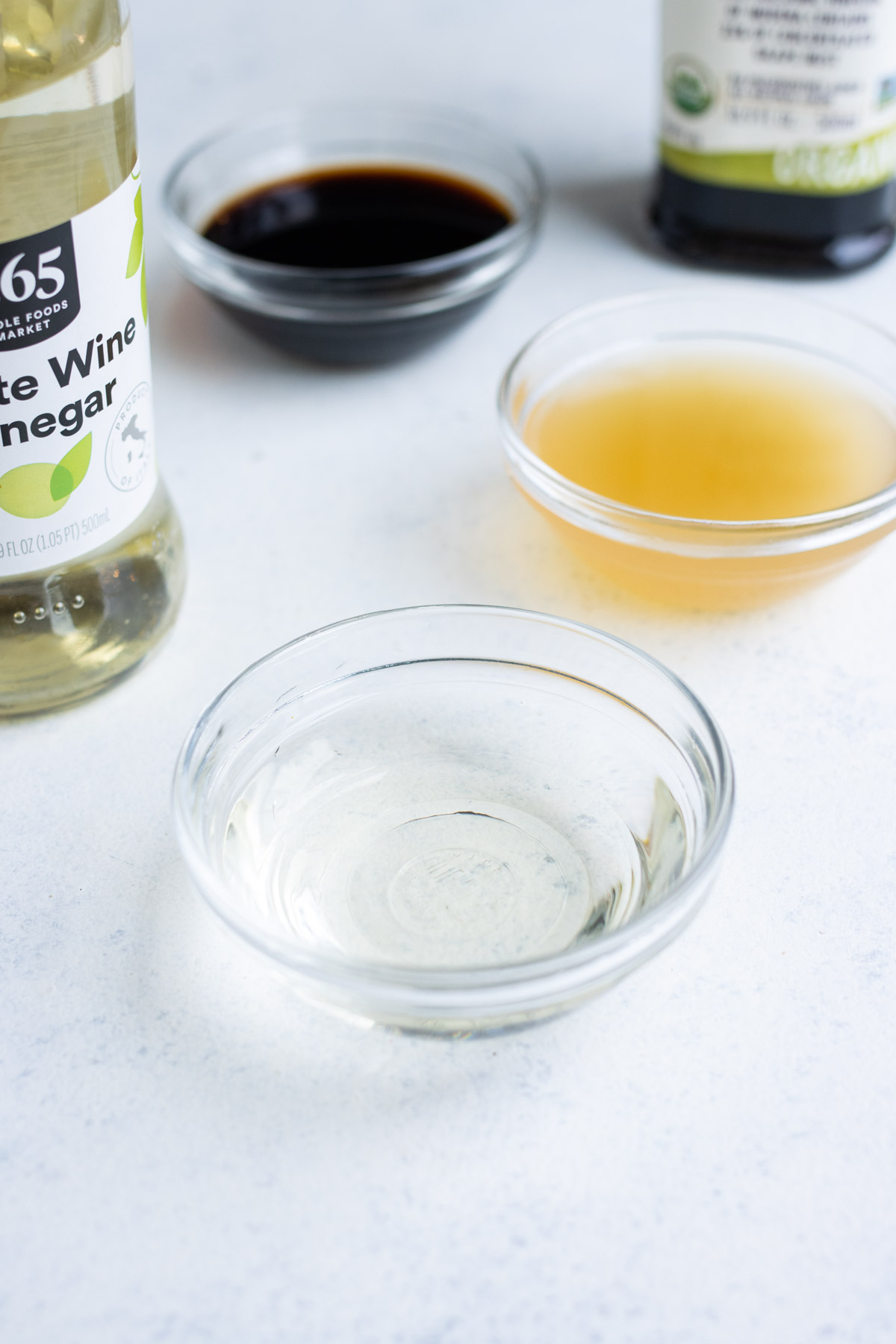 Close-up of white wine vinegar in a small, glass bowl with other vinegars in the background.