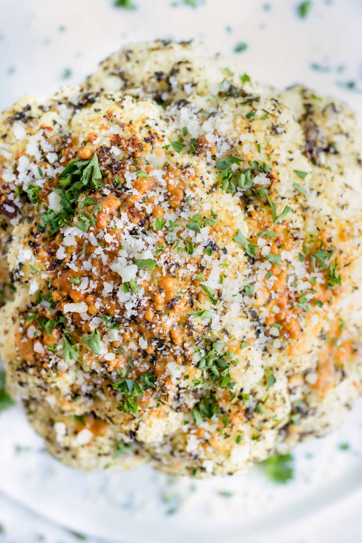 Overhead shot of a paleo approved whole roasted cauliflower surrounded by a green garnish.