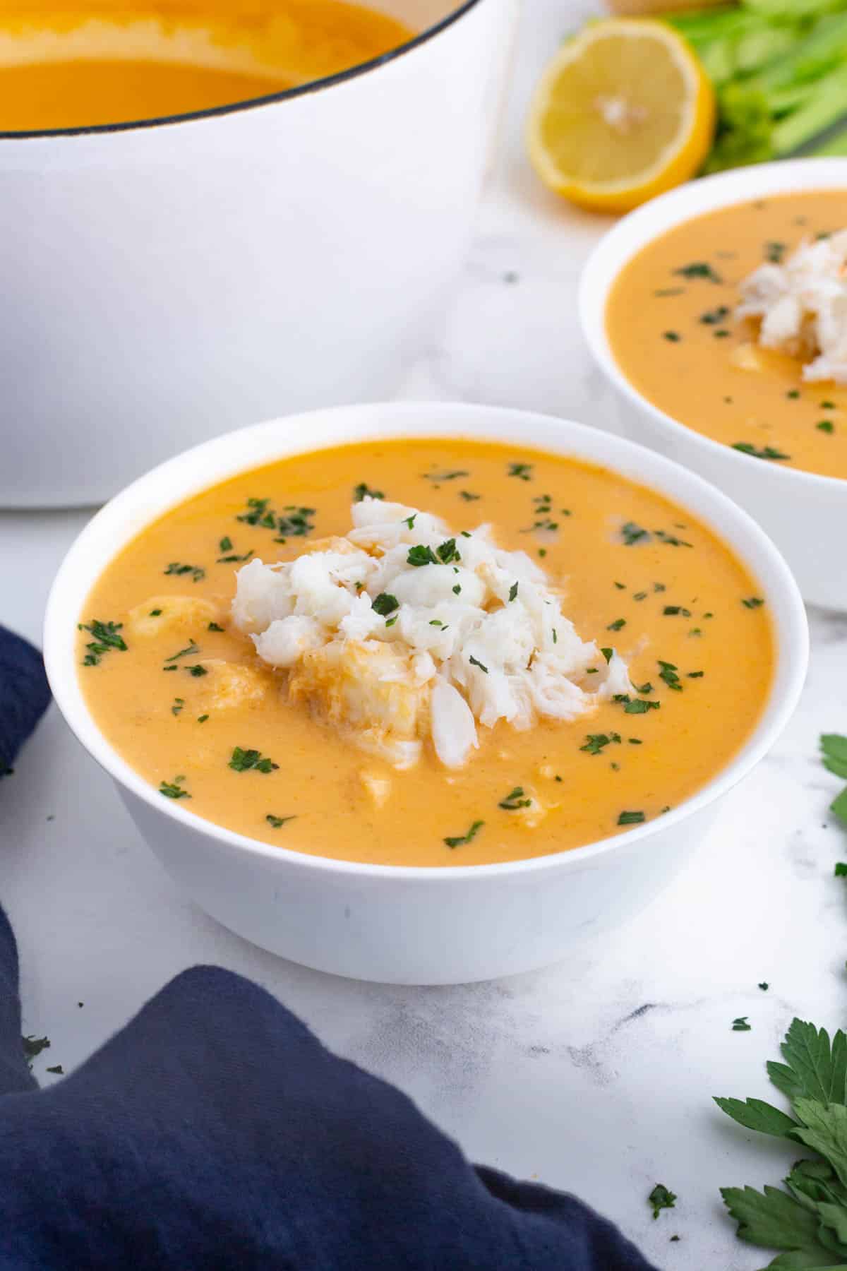 Two bowls with crab bisque next to the pot.