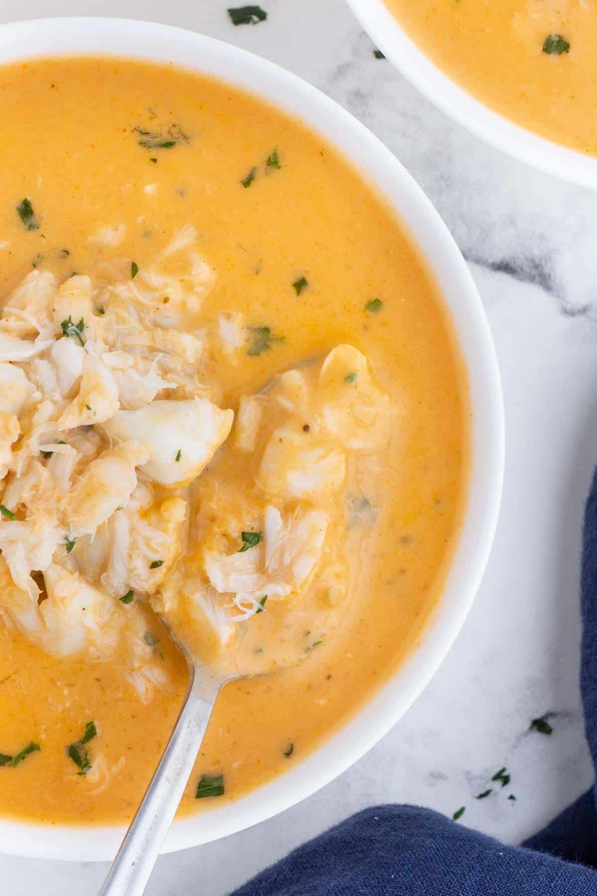 A spoon scoops out crab bisque with chunks of crab from a white a bowl.