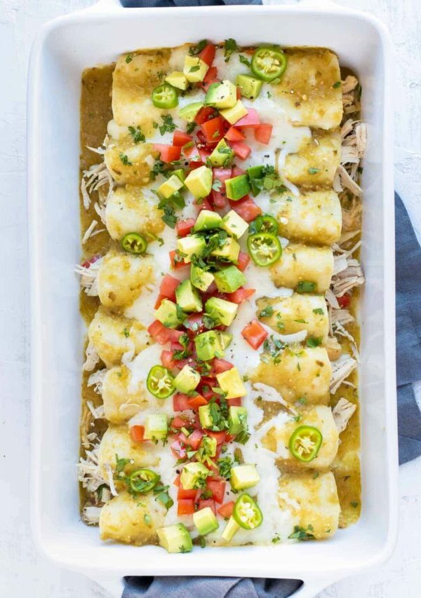 A baking dish full of salsa verde chicken enchiladas in a white baking pan with a grey towel.