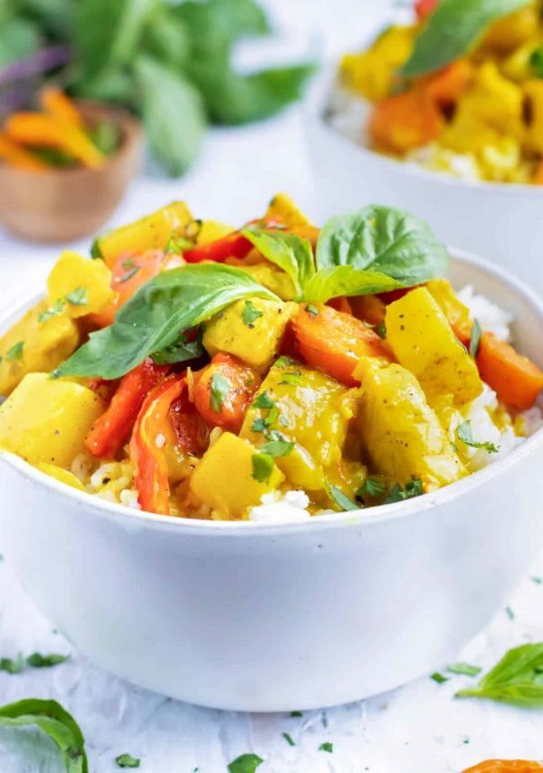 A white serving bowl of Thai curry that is made with yellow curry paste, chicken, potatoes, and carrots.