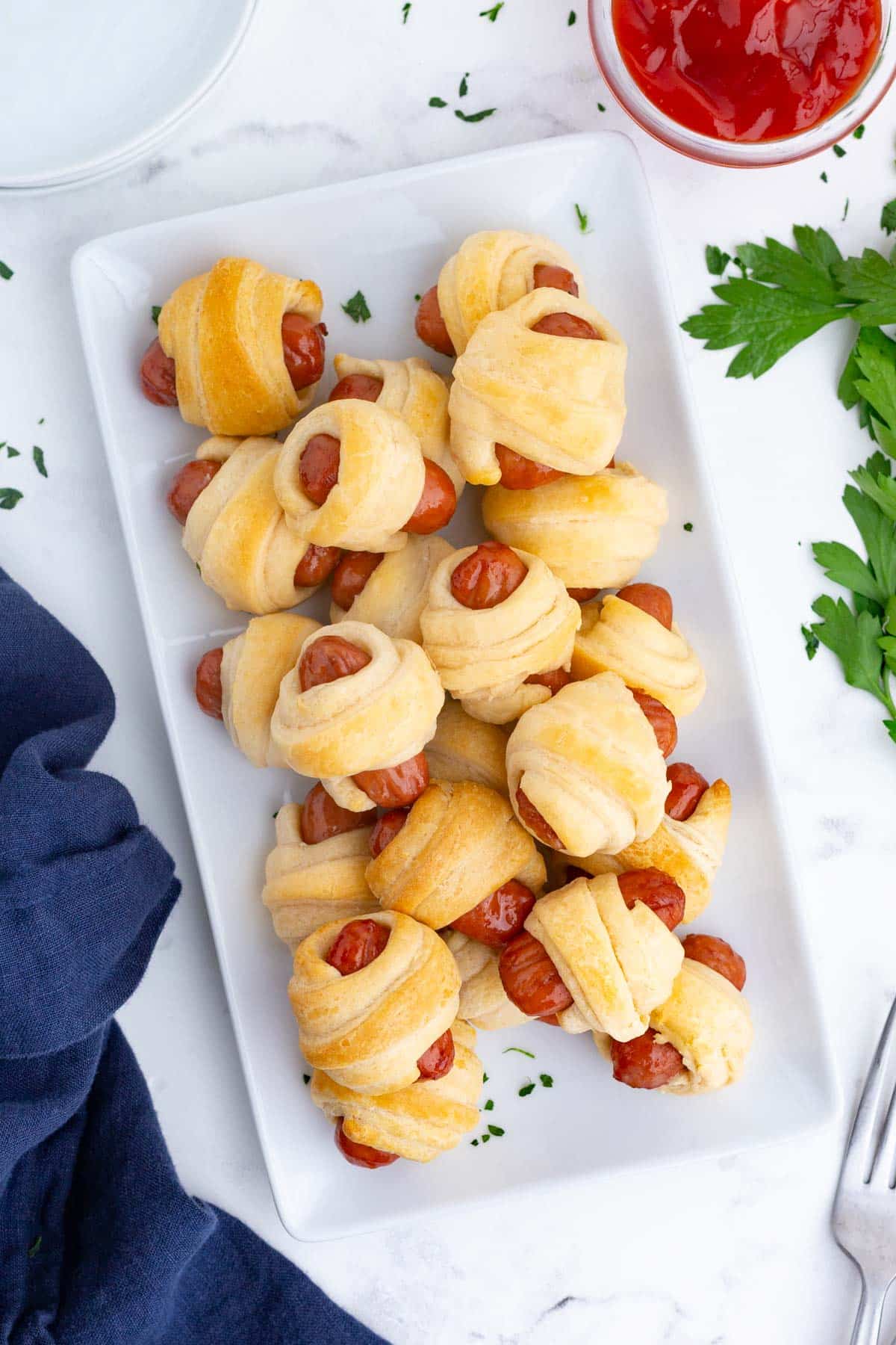 A long, rectangular plate with pigs in a blanket is served for breakfast.