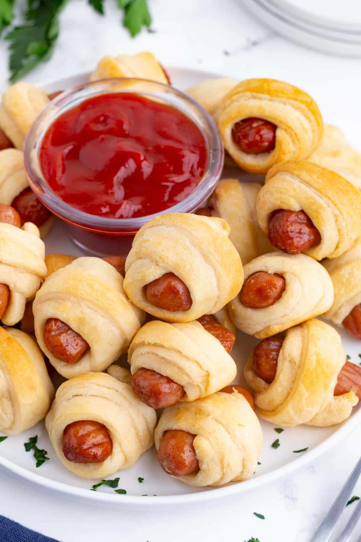 Pigs in a blanket, wrapped in crescent rolls, are served with a dish of ketchup.